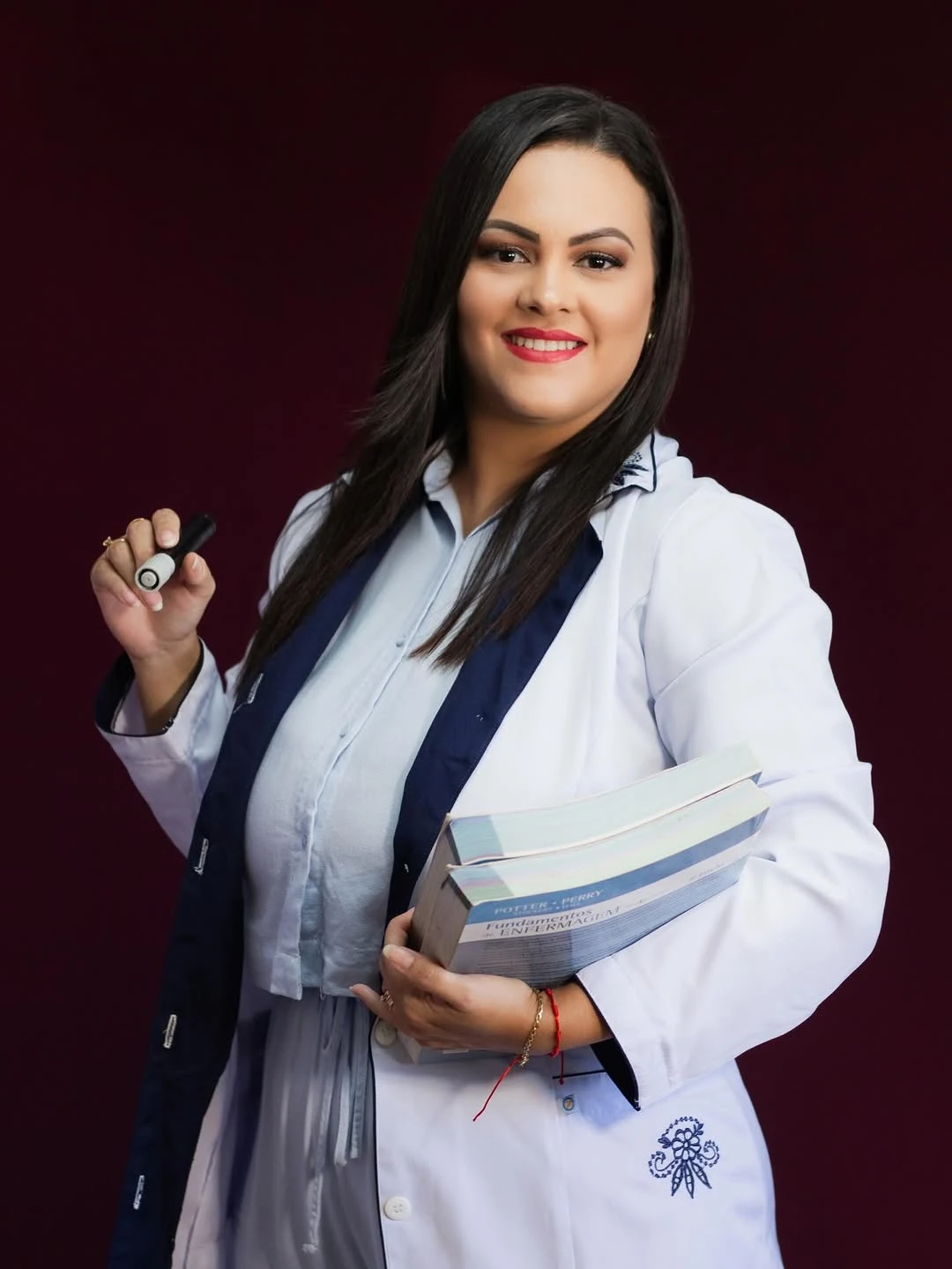 Camila Araújo de jaleco, segurando livros de enfermagem